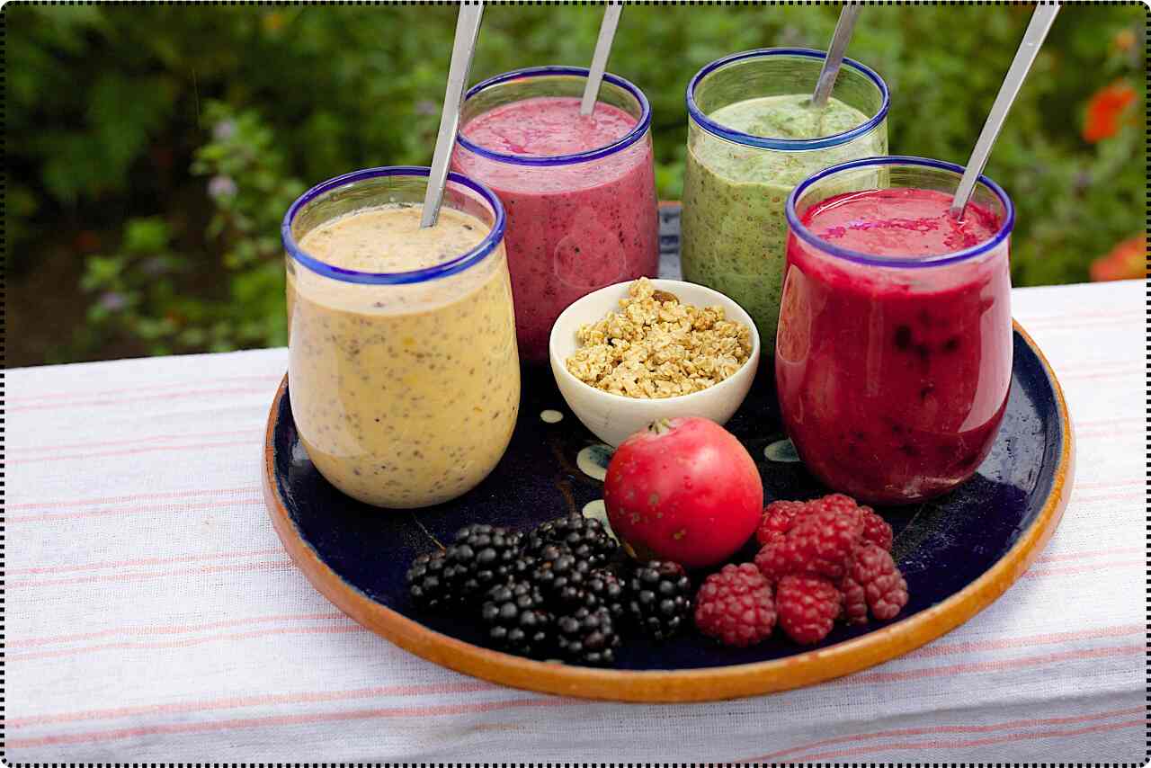 Colorful assortment of freshly squeezed fruit juices in tall glasses, including pineapple and watermelon.